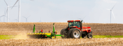 A tractor in a large field, with wind turbines in the background