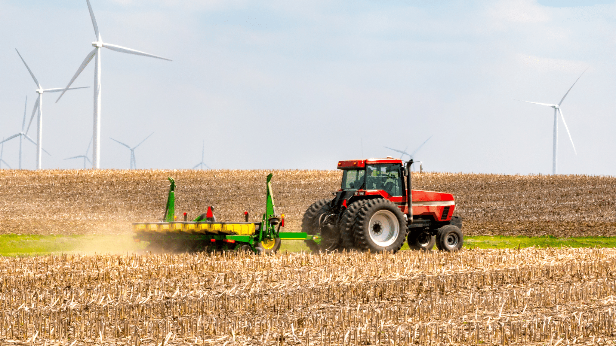 A tractor in a large field, with wind turbines in the background