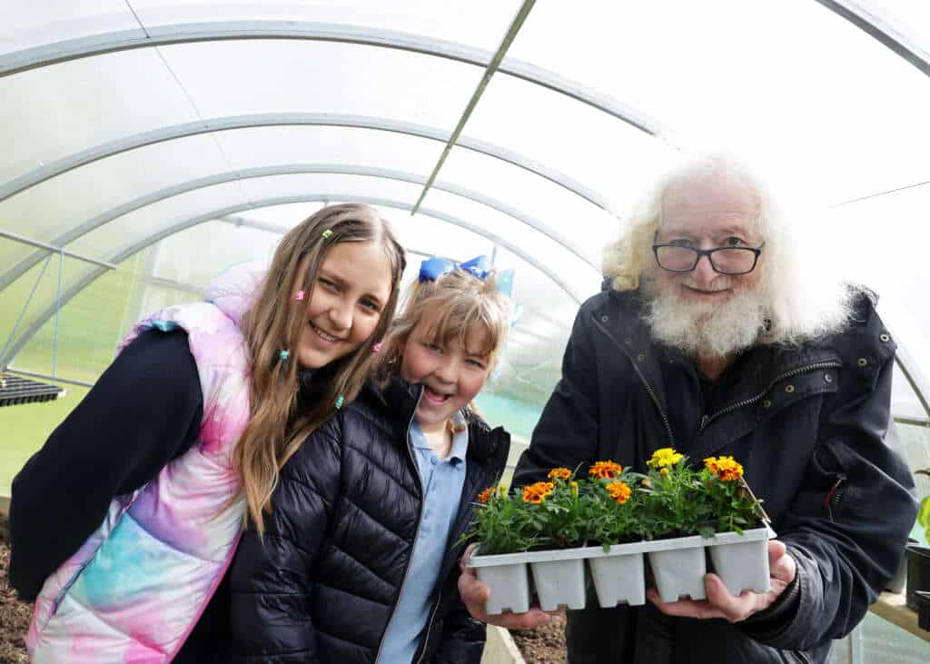 Three people with flowers in a polytunnel - two school children and an older man